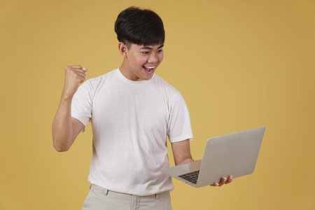 portrait of happy glad rejoicing cheerful young asian man dressed casually holding laptop computer...