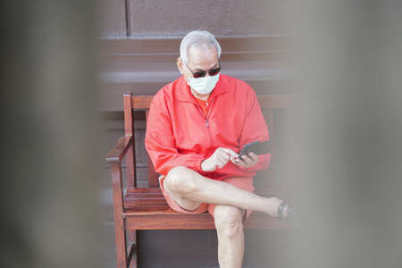 asian old elder senior man elderly male wearing face mask using mobile smart phone cellphone outdoor. mature retirement lifestyleの写真素材