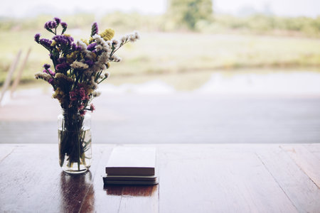 flower bouquet in glass vase and book on wooden table at patio