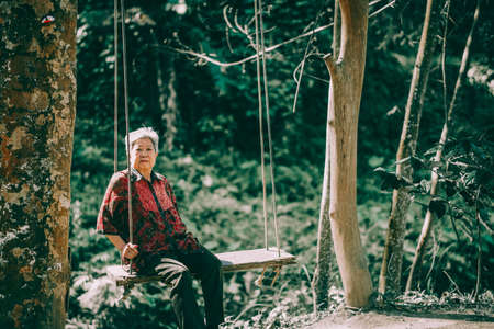 asian old elderly female elder woman resting relaxing on swing in garden. senior leisure lifestyleの写真素材