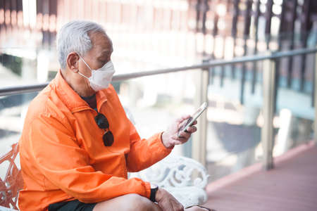 asian old elder senior man elderly wearing mask using mobile smart phone cellphone outdoor. mature retirement lifestyleの写真素材