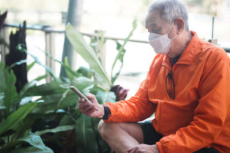 asian old elder senior man elderly wearing mask using mobile smart phone cellphone outdoor. mature retirement lifestyleの写真素材
