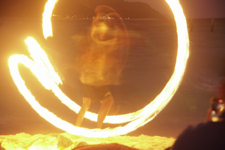 man performing fire show dancing with flame on beach at nightの写真素材