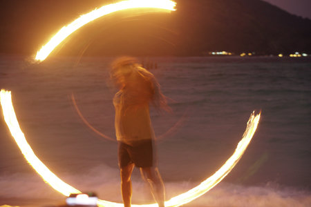 man performing fire show dancing with flame on beach at nightの写真素材