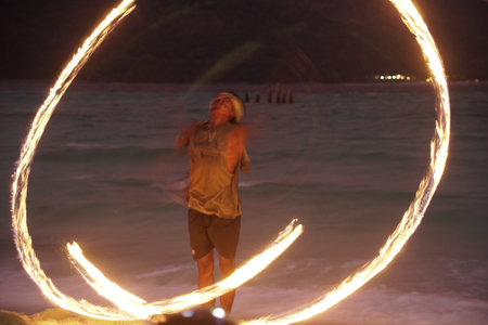 man performing fire show dancing with flame on beach at nightの写真素材