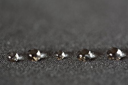 A background/desktop picture of 5 water drops in a row on a dark textured surfaceの写真素材