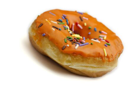 A donut with orange frosting and rainbow sprinkles against a white backgroundの写真素材
