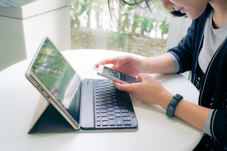 Young student women wearing smart band touching smart phone while using tablet computerの写真素材