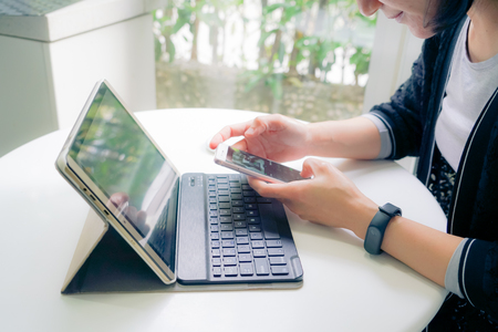 Young student women wearing smart band touching smart phone while using tablet computerの写真素材