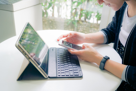 Young student women wearing smart band touching smart phone while using tablet computerの写真素材