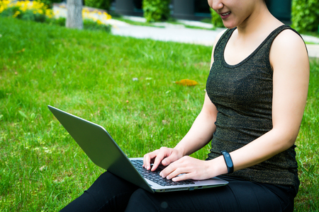 A young woman sitting on the grass is using laptop computerの写真素材