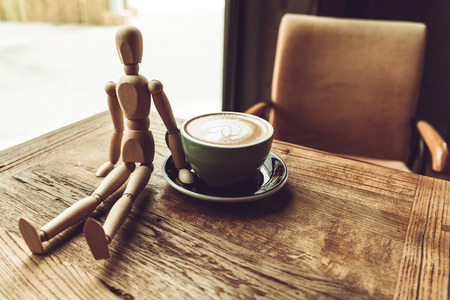 a wood man sitting and touch the hot mocha coffee or capuchino in the green cup on the wooden tableの写真素材