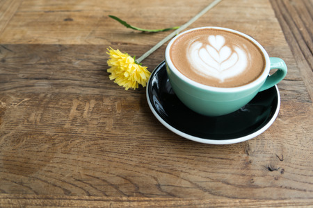 Hot mocha coffee or capuchino in the green cup with heart pattern and yellow flower on the wooden tableの写真素材