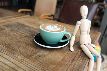 Hot mocha coffee or capuchino in the green cup with a wood man sitting on the wooden tableの写真素材