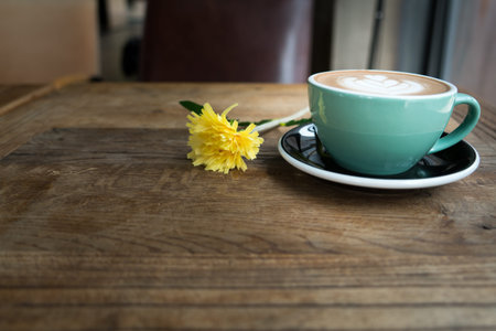 Hot mocha coffee or capuchino in the green cup with heart pattern and yellow flower on the wooden...