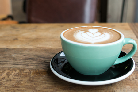 Hot mocha coffee or capuchino in the green cup with heart pattern on the wooden tableの写真素材