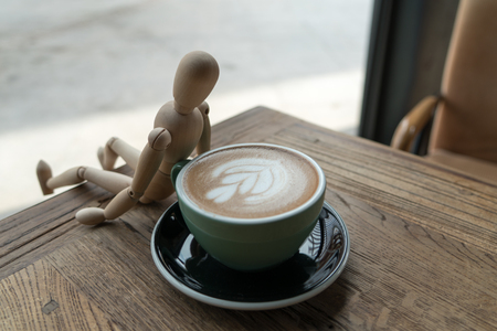 Hot mocha coffee or capuchino in the green cup lean by wood man on the wooden tableの写真素材