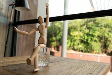 wood man is sitting on a glass of water while raise hand upの写真素材