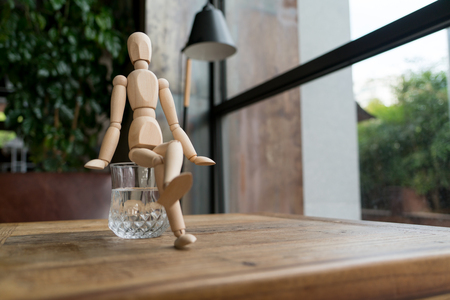 wood man is sitting on a glass of waterの写真素材