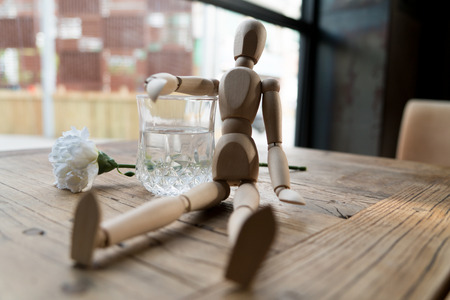 a wood man is sitting and put the arm on the glass of waterの写真素材