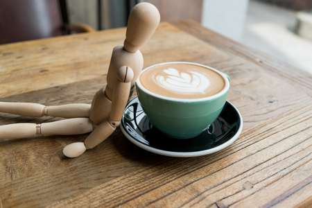 Hot mocha coffee or capuchino in the green cup lean by wood man on the wooden tableの写真素材