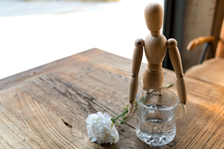 wood man is trying to hold on a glass with white carnation on the wooden tableの写真素材