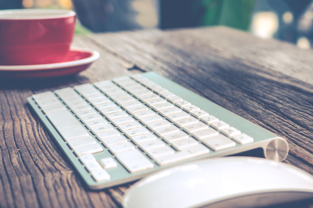 focus on English alphabet of the while keyboard with mouse and red cup of coffeeの写真素材