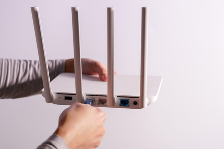 The back view of router showing the lan internet port, and the hand is pluging in the land cable on a white routerの写真素材