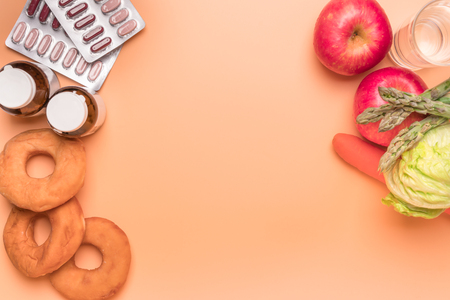 healthcare and medical concept medicine with junk bakery with the fresh vegetable and fruit on the orange background with copy spaceの写真素材