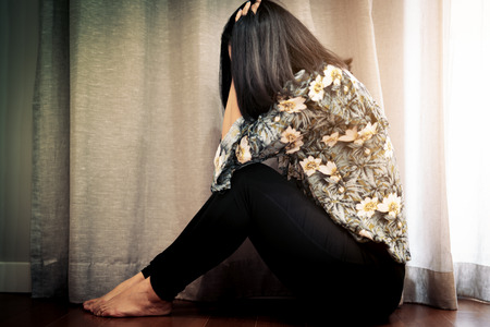 depressed women sitting near curtain in living room, alone, sadness, emotional conceptの写真素材