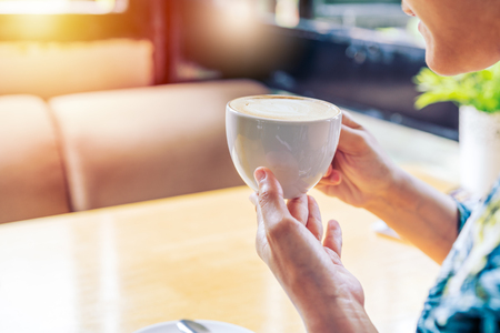 women hands holding hot cup of coffee or tea in morning sunlightの写真素材