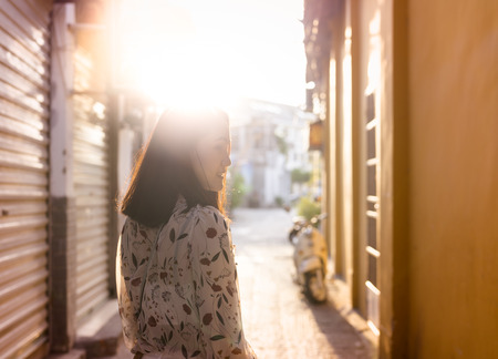 Woman walking on walkway in narrow of village urban landscape at the sunset, looking to the sideの写真素材