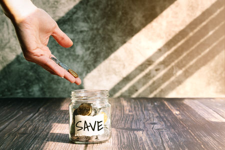 save money, woman put coins in glass jar for money saving financial conceptの写真素材