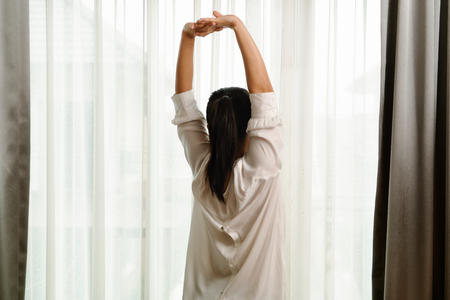 Woman stretching in bedroom after wake up, back viewの写真素材