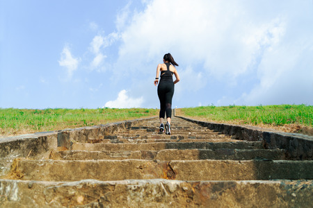 young sport woman running outdoor upstairs on blue skyの写真素材