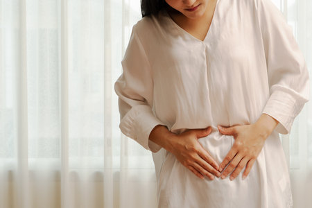 Young woman suffering from abdominal pain feeling stomachache, symptom of pms on white backgroundの写真素材
