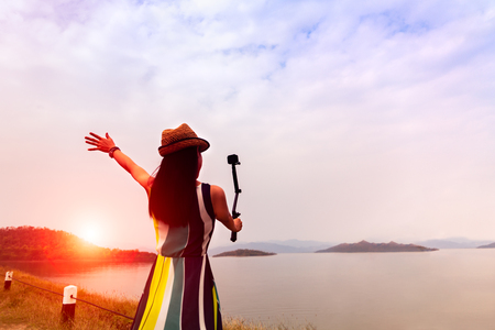 traveler woman enjoy take a selfie at beautiful sunset on the lake with mountains on backgroundの写真素材