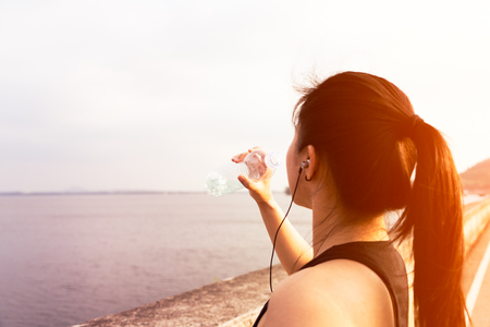 Sport woman standing on the bay and drinking water after runningの写真素材
