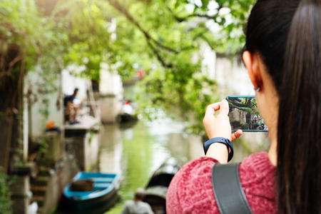 young woman having fun in local canal city in China with camera on smartphone making picturesの写真素材