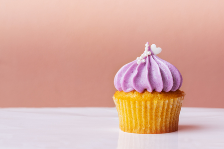 Happy Mothers Day, cute cupcake with small white heart on purple cream on pink backgroundの写真素材
