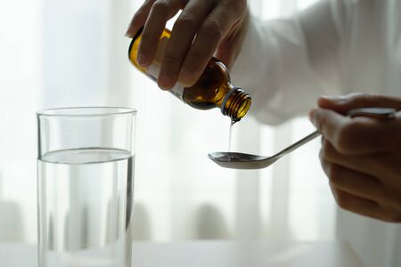 Woman hand pouring medication or cough syrup from bottle to spoon. healthcare conceptの写真素材