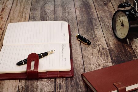 Retro alarm clock with memo book and luxury pen on wooden tableの写真素材