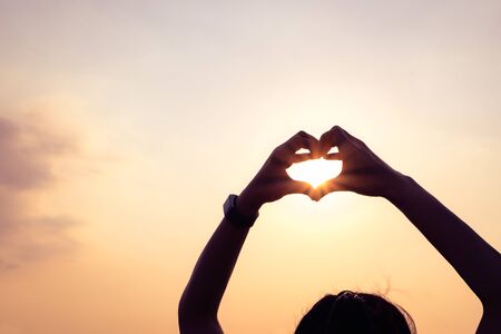 hands forming a heart shape with sunset silhouetteの写真素材
