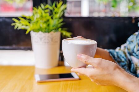 women hands holding hot cup of coffee or tea in morning sunlightの写真素材