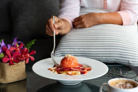 old woman hold folk with freshly homemade Pancakes Strawberry Crumble on white dessert plateの写真素材