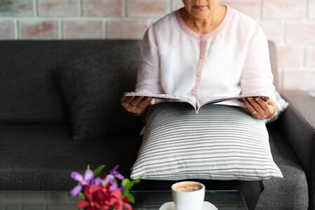 old woman reading a book with cup of coffee at homeの写真素材