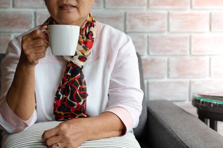 Old woman hold a cup of hot coffee drink at homeの写真素材