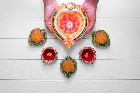 Happy Diwali - Clay Diya lamps lit during Diwali, Hindu festival of lights celebration. Colorful traditional oil lamp diya on white wooden backgroundの写真素材
