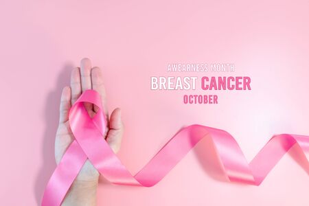 Pink ribbon symbol. Breast Cancer Awareness Month Campaign. Woman hand hold the pink ribbon on pink backgroundの写真素材