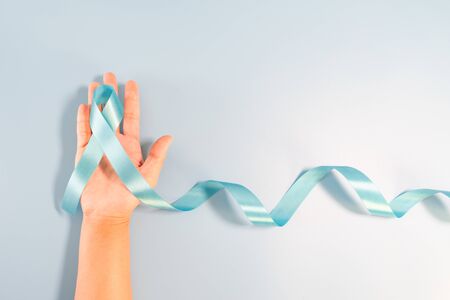 Prostate cancer awareness campaign concept, Men's health concept. hand holding light blue ribbon long tail on blue background. Symbol for support men who living with cancerの写真素材